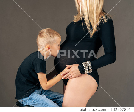 Sweet family moment boy kisses his pregnant mothers belly, showing love and excitement for the unborn baby. Studio maternity concept 132307805