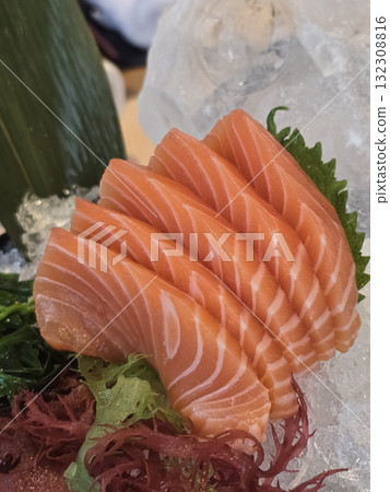 Fresh salmon sashimi served on ice with garnishes, showcasing vibrant colors and textures. This dish highlights delicate layers of fish, perfect for sushi lovers 132308816