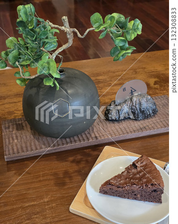 decorative arrangement featuring black ceramic vase, slice of chocolate cake, and small plant. setting is warm and inviting, perfect for cozy cafe experience 132308833