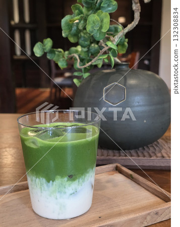refreshing green tea drink with layered milk, served in glass, alongside decorative plant and ceramic pot, creating serene atmosphere 132308834