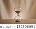 A simple hourglass on a wooden table with a beige backdrop, symbolizing time flow and minimalistic living. Represents timeless themes in a creative, uncluttered presentation for stylish concepts. 132308991