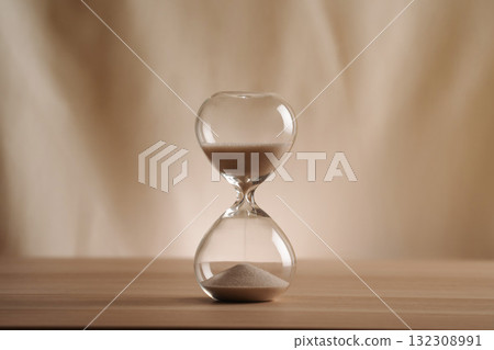A simple hourglass on a wooden table with a beige backdrop, symbolizing time flow and minimalistic living. Represents timeless themes in a creative, uncluttered presentation for stylish concepts. 132308991