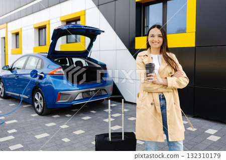 Young woman with cup of coffee waiting while her electric car charging, sustainable and economic transportation concept 132310179