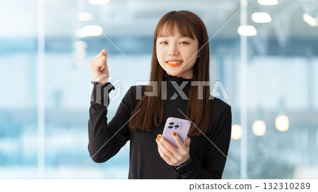 A woman/businesswoman holding a smartphone and making a fist pump A woman/businesswoman holding a smartphone and making a fist pump 132310289