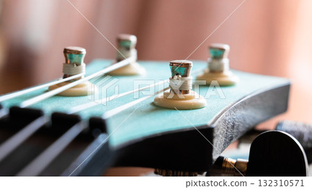 Close-up of a guitar headstock with tuning pegs and strings. The headstock is turquoise with metallic components. The background is softly blurred.	 132310571