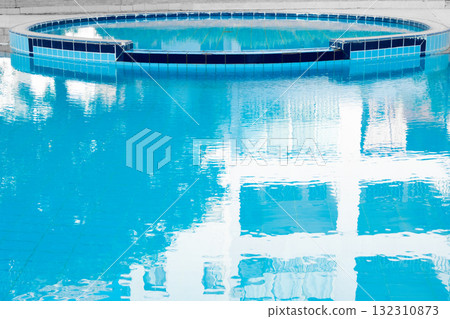A serene swimming pool with clear blue water, surrounded by palm trees and landscaped gardens. The pool features a curved design and tiled edges. 132310873