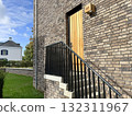 brick house exterior with wooden door, staircase and black metal railing 132311967