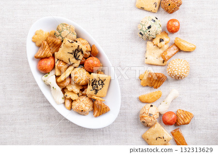 Japanese rice crackers, in white bowl, on linen. Assorted varieties of Arare crackers made from baked rice flour, brushed with soy sauce and vinegar for a smooth texture, some sprinkled with seaweed. Japanese rice crackers, in white bowl, on linen. Assorted varieties of Arare crackers made from baked rice flour, brushed with soy sauce and vinegar for a smooth texture, some sprinkled with seaweed. 132313629