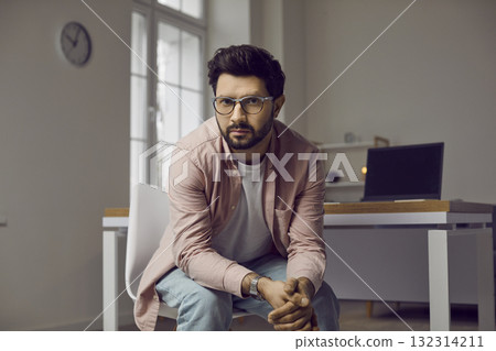 Portrait of serious and confident male freelancer who poses in his small office. 132314211
