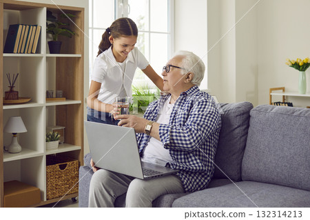 Child helps grandfather at home and gives him glass of water while he is sitting on sofa Child helps grandfather at home and gives him glass of water while he is sitting on sofa 132314213