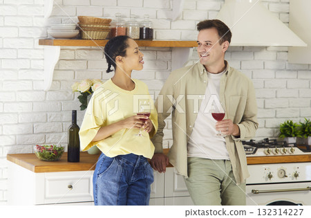 Happy couple relaxing with wine in cozy kitchen, smiling and talking together Happy couple relaxing with wine in cozy kitchen, smiling and talking together 132314227
