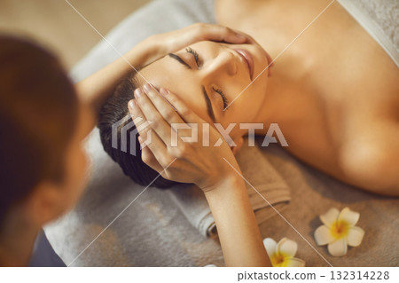 Beautiful woman enjoying facial treatment and head massage while relaxing in spa salon Beautiful woman enjoying facial treatment and head massage while relaxing in spa salon 132314228