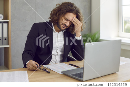 Tired man suffering from headache working on his workplace, massaging his forehead. 132314259