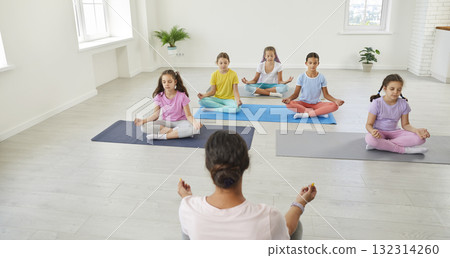 Group of children having a yoga class, sitting on mats, doing relaxing exercises and mediating Group of children having a yoga class, sitting on mats, doing relaxing exercises and mediating 132314260