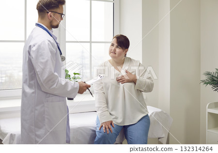 Fat woman sitting in the doctor's office pointing to her chest during medical examination in clinic Fat woman sitting in the doctor's office pointing to her chest during medical examination in clinic 132314264
