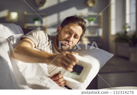 Sleepy man lying on bed and stopping alarm clock 132314278