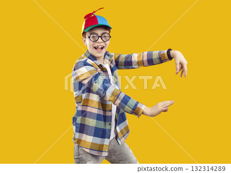 Happy funny child in shirt, propeller cap and glasses dancing on orange background 132314289