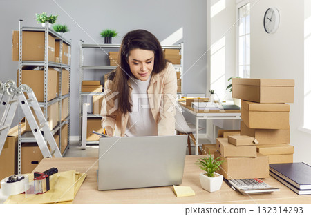 Woman Conducting Parcel Inventory In Post Office Warehouse Using Laptop 132314293