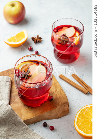 A cranberry drink in a two glasses on a wooden board on a light background with cinnamon and napkin. A cranberry drink in a two glasses on a wooden board on a light background with cinnamon and napkin. 132314665
