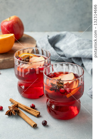 A cranberry drink in a two glasses on a light background with cinnamon, berries and fruits. A cranberry drink in a two glasses on a light background with cinnamon, berries and fruits. 132314666