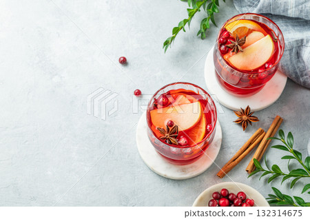 A cranberry drink in a two glasses on a light background with cinnamon, berries and green branch. A cranberry drink in a two glasses on a light background with cinnamon, berries and green branch. 132314675