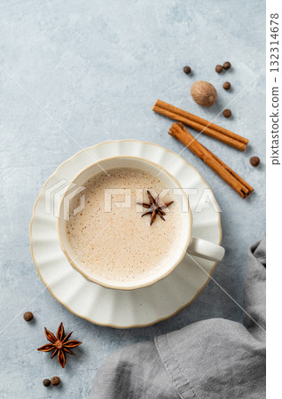 Traditional Indian masala chai tea with milk and spices in a white cup on a light blue background 132314678