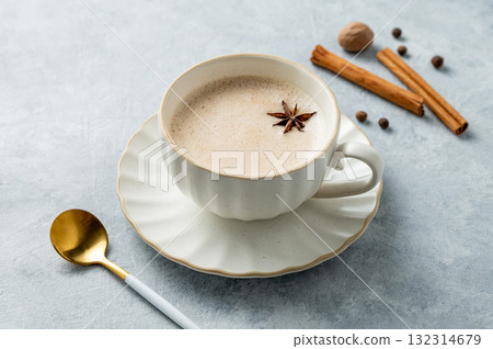 Traditional Indian masala chai tea with milk and spices in a white cup on a light background  132314679