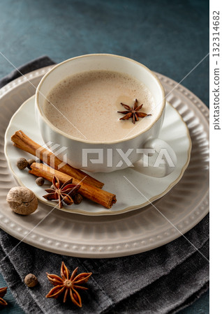 Traditional Indian masala chai tea with milk and spices in a white cup on a dark background 132314682