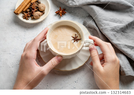 Hands holding traditional Indian masala chai tea with milk and spices in a white cup 132314683
