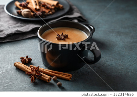 Traditional Indian masala chai tea with milk and spices in a black cup on a dark background close up 132314686