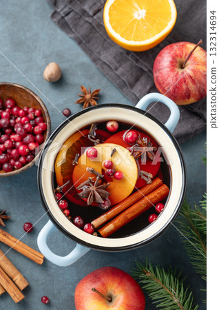 A pot of red mulled wine with spices, orange, apple slices and cranberries on a dark blue background A pot of red mulled wine with spices, orange, apple slices and cranberries on a dark blue background 132314694