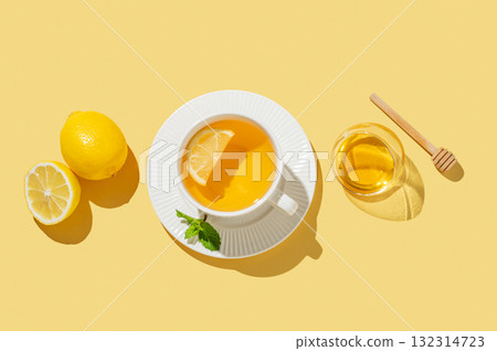 Flat lay of hot tea with lemon, honey, and mint in a cup on a bright yellow background with citrus Flat lay of hot tea with lemon, honey, and mint in a cup on a bright yellow background with citrus 132314723
