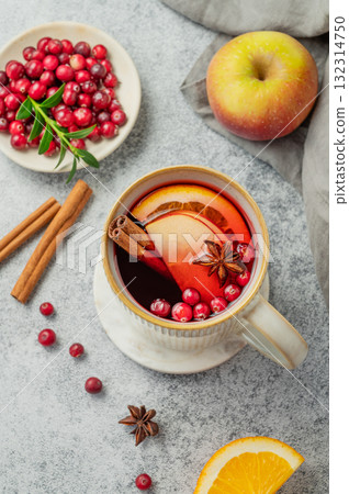A hot cranberry Christmas drink in a mug on a gray background with cinnamon, berries and fruits. A hot cranberry Christmas drink in a mug on a gray background with cinnamon, berries and fruits. 132314750