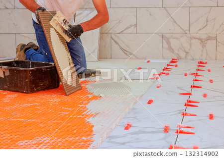 Worker installs marble tiles on bathroom floor using mortar spacers for alignment. Worker installs marble tiles on bathroom floor using mortar spacers for alignment. 132314902