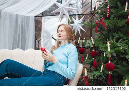 Upset blonde Caucasian woman reading bad news on smartphone near Christmas tree Upset blonde Caucasian woman reading bad news on smartphone near Christmas tree 132315102