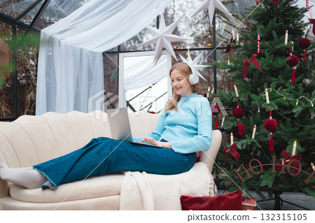 Smiling blonde Caucasian woman working on laptop near Christmas tree 132315105