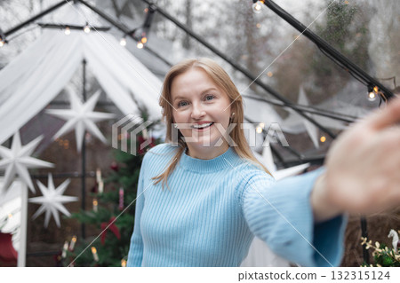 Portrait of attractive cheerful blonde Caucasian woman taking selfie in festive Christmas interior 132315124