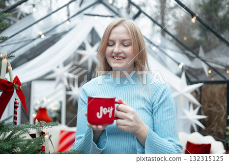Blonde woman enjoying hot drink from red Christmas mug 132315125