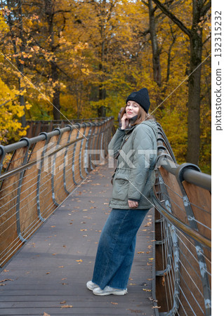 A woman in a green jacket and black hat leans on a wooden bridge in VDNH park, closing her eyes and enjoying the autumn sun A woman in a green jacket and black hat leans on a wooden bridge in VDNH park, closing her eyes and enjoying the autumn sun 132315232