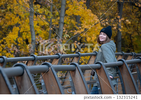 A woman in a green jacket and black hat leans on a wooden bridge in VDNH park, closing her eyes and enjoying the autumn sun A woman in a green jacket and black hat leans on a wooden bridge in VDNH park, closing her eyes and enjoying the autumn sun 132315241
