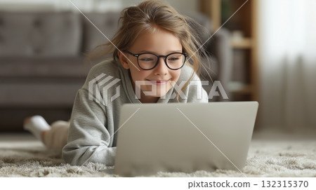 A cheerful young girl uses a laptop in a home setting 132315370