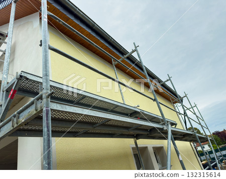 Yellow house renovation in progress with scaffolding under a cloudy sky at midday 132315614