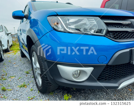 Bright blue car parked in a gravel lot under an overcast sky, showcasing modern design and sleek features during a cloudy day in an urban setting 132315625
