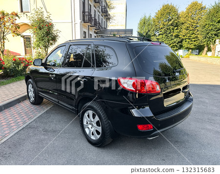 Sleek black SUV parked near a modern building with lush greenery under a clear blue sky in a quiet neighborhood setting Sleek black SUV parked near a modern building with lush greenery under a clear blue sky in a quiet neighborhood setting 132315683