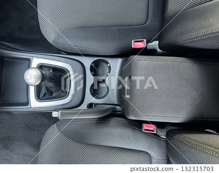 Close-up view of car interior showing gear shift, center console, and cup holders in a modern vehicle with sleek design and dark upholstery Close-up view of car interior showing gear shift, center console, and cup holders in a modern vehicle with sleek design and dark upholstery 132315703