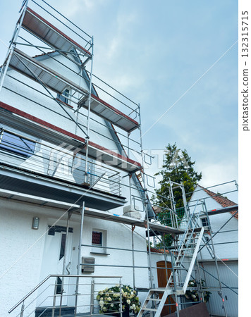 Renovation project underway on a charming white house surrounded by scaffolding under a cloudy sky in a quiet neighborhood 132315715