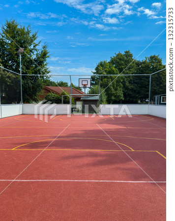 Bright sunny day on an outdoor basketball court in a park surrounded by trees and blue skies 132315733