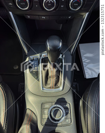 Modern car console showcasing gear shift, multimedia controls, and leather detailing in bright sunlight, highlighting the sleek design and advanced features 132315751