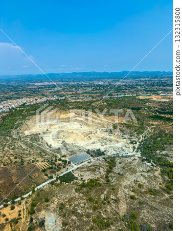 Vast quarry landscape viewed from above showing earthworks, vegetation, and distant hills under a clear blue sky Vast quarry landscape viewed from above showing earthworks, vegetation, and distant hills under a clear blue sky 132315800