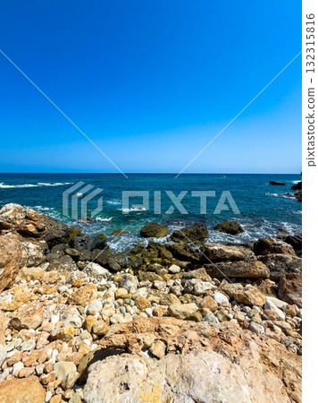 Bright blue ocean waves crash against rocky shores under a clear sky on a peaceful summer day by the sea 132315816